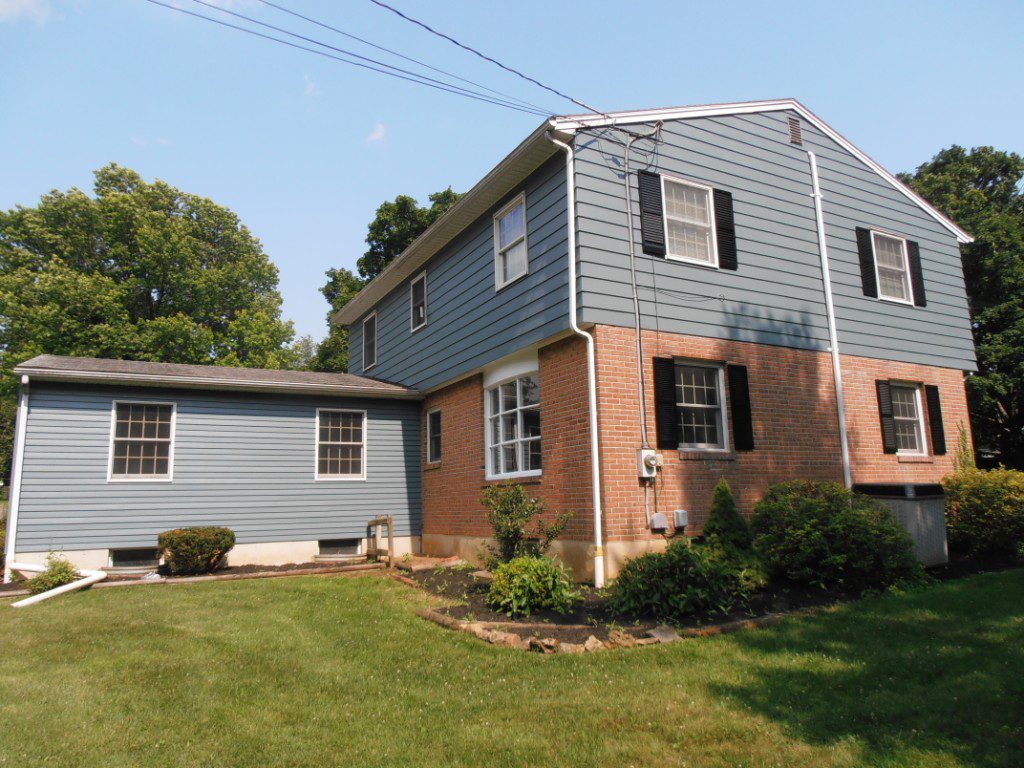 Two-story house with brick and blue siding under a clear sky.