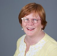 Smiling person with glasses and short hair.